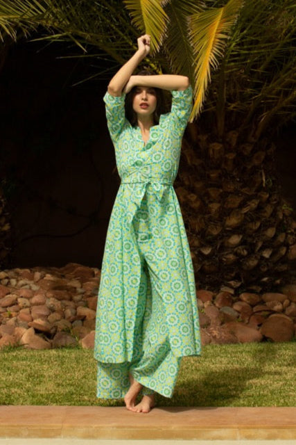 Woman in a green patterned dress standing by a pool with palm trees in the background